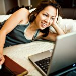 девушка, улыбаясь, смотрит в ноутбук