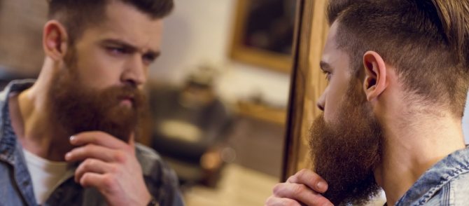 мужчина смотрит в зеркало и трогает бороду